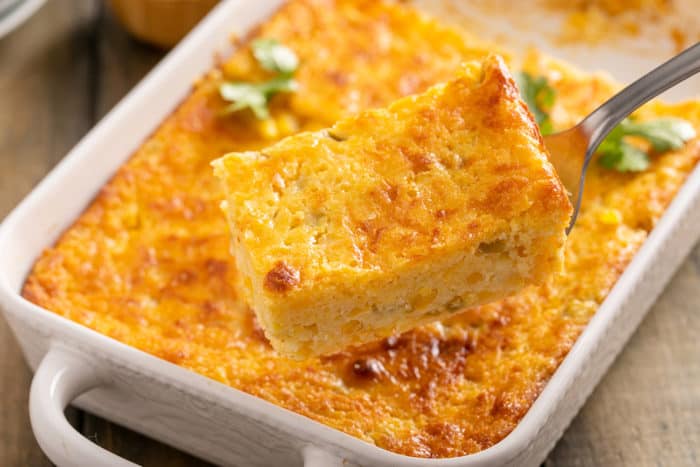 Piece of green chile corn casserole being served out of a white baking dish