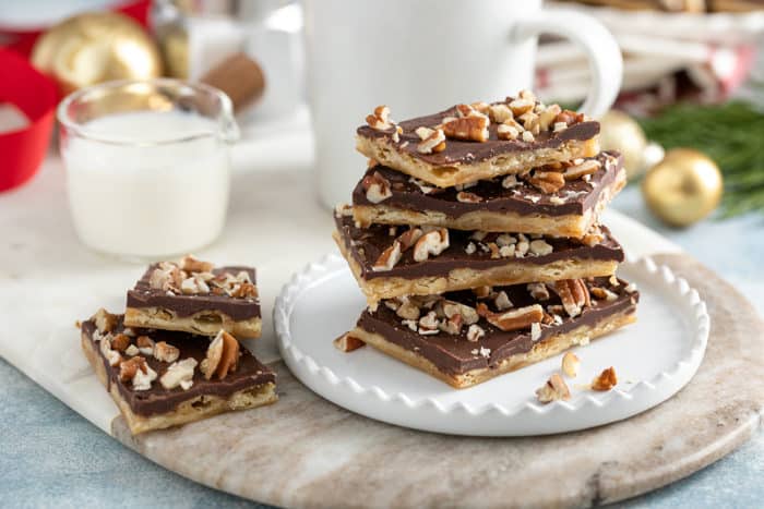 Four pieces of saltine toffee stacked on a white plate in front of a cup of coffee