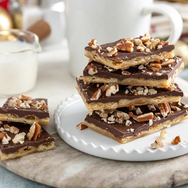 Four pieces of saltine toffee stacked on a white plate in front of a cup of coffee