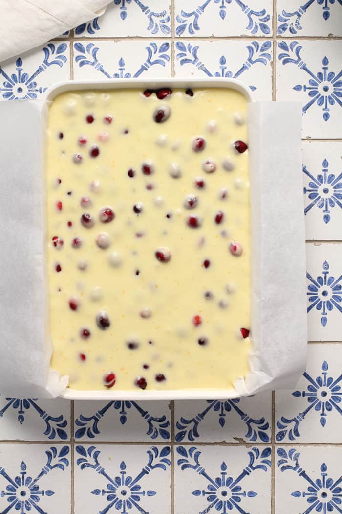 Unbaked cranberry gooey butter bars in a parchment-lined baking dish