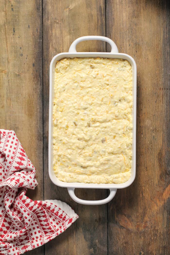 Batter for green chile corn casserole in a white baking dish, ready to go in the oven