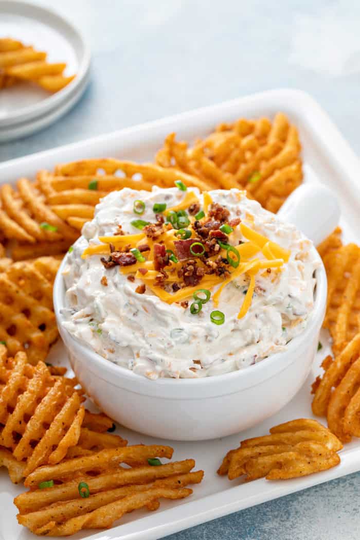 Bowl of loaded baked potato dip on a platter of waffle fries