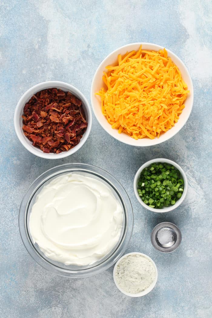 Ingredients for loaded baked potato dip arranged on a blue countertop