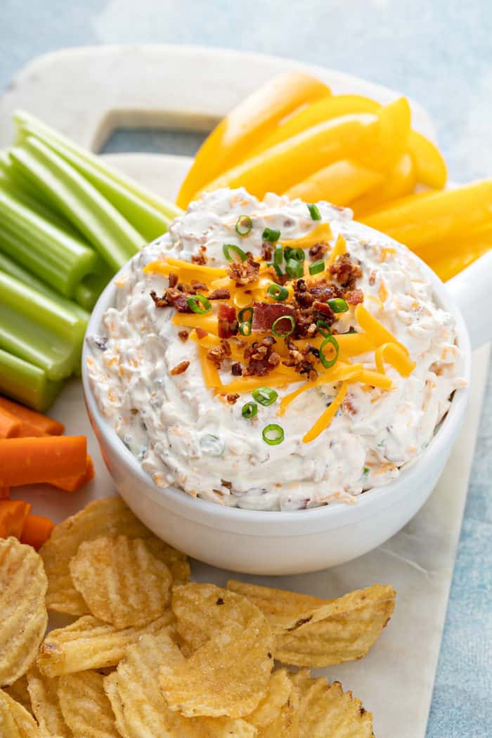 Bowl of baked potato dip on a white platter next to chips and fresh veggies