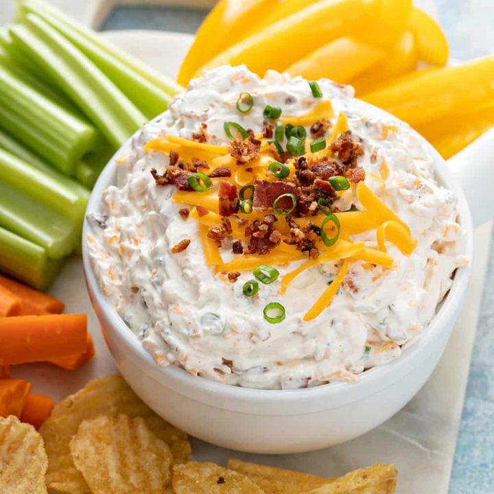 Bowl of baked potato dip on a white platter next to chips and fresh veggies