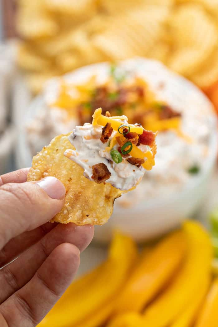 Hand holding up a potato chip dipped in loaded baked potato dip