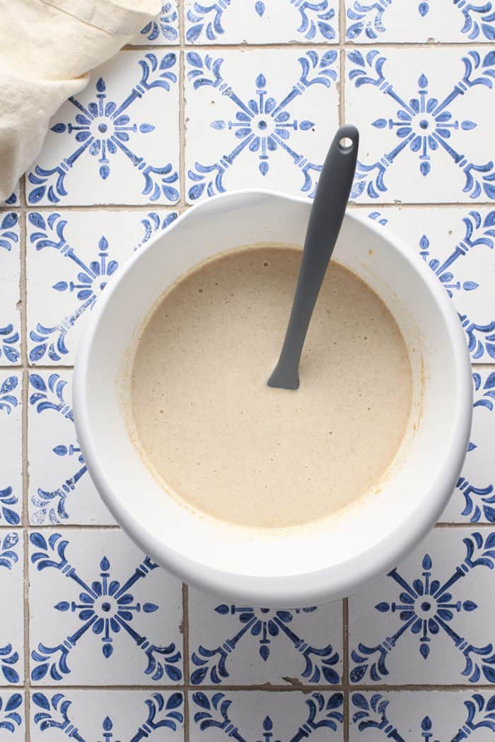 Custard for croissant bread pudding in a white mixing bowl on a blue-and-white tiled countertop