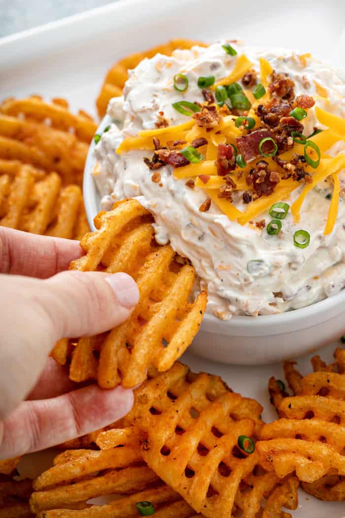 Hand dipping a waffle fry into loaded baked potato dip