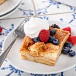 Plated slice of croissant bread pudding topped with fresh berries and whipped cream