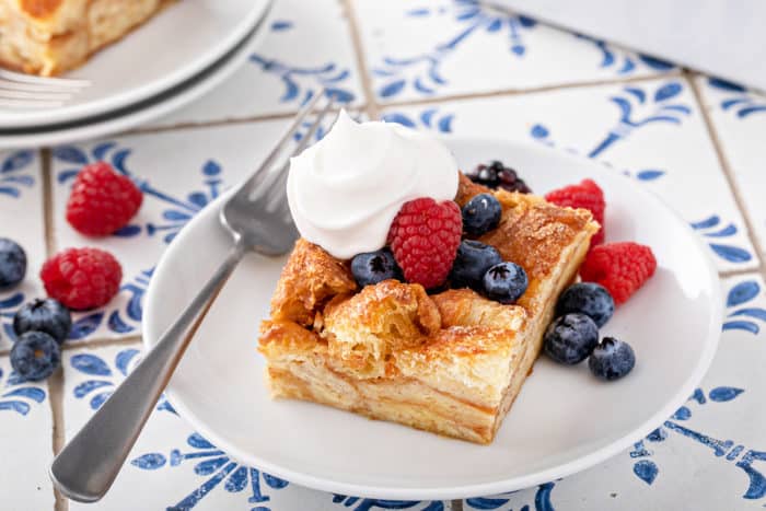 Plated slice of croissant bread pudding topped with fresh berries and whipped cream