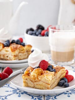 Two plates with slices of croissant bread pudding, topped with whipped cream and fresh berries