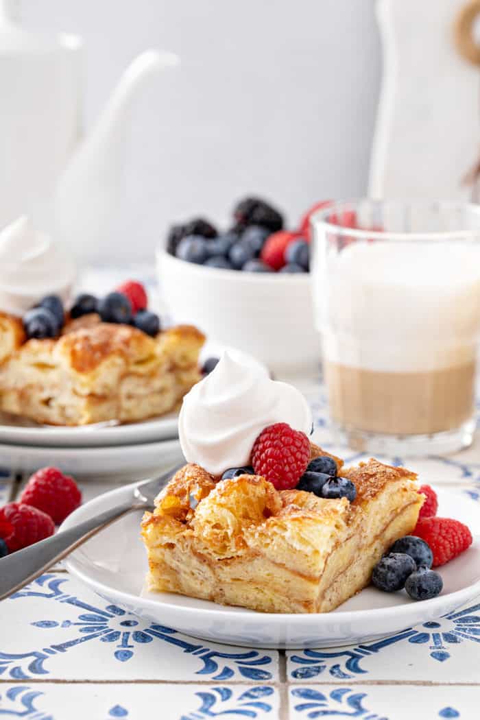 Two plates with slices of croissant bread pudding, topped with whipped cream and fresh berries