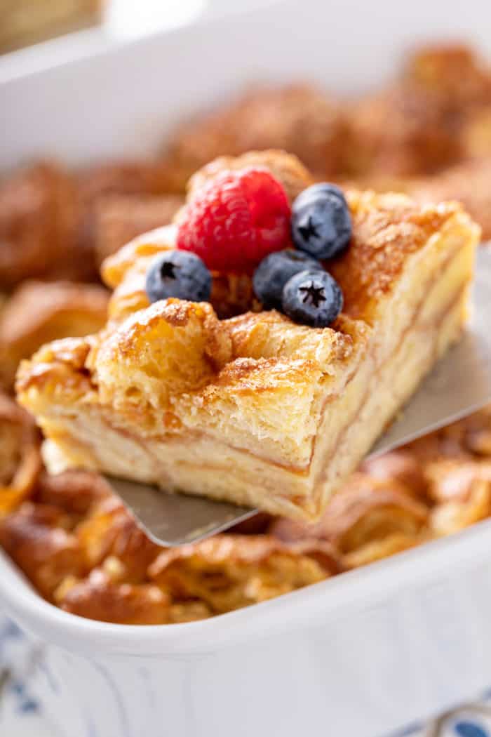 Spatula holding up a slice of croissant bread pudding, topped with fresh berries