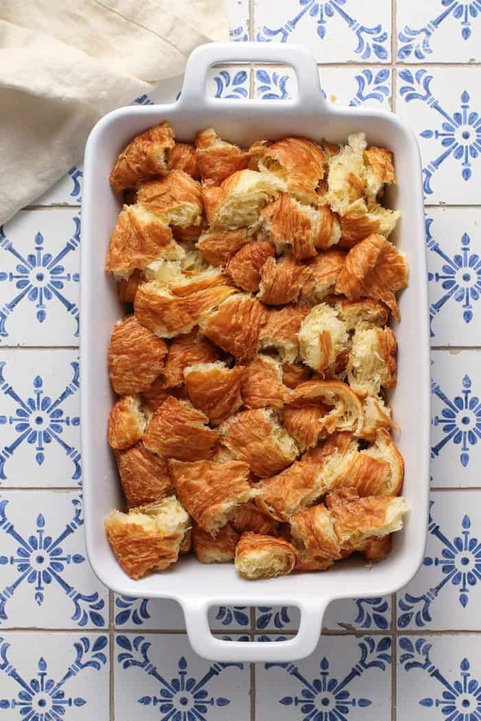 Croissant bread pudding in a white casserole dish, ready to be baked