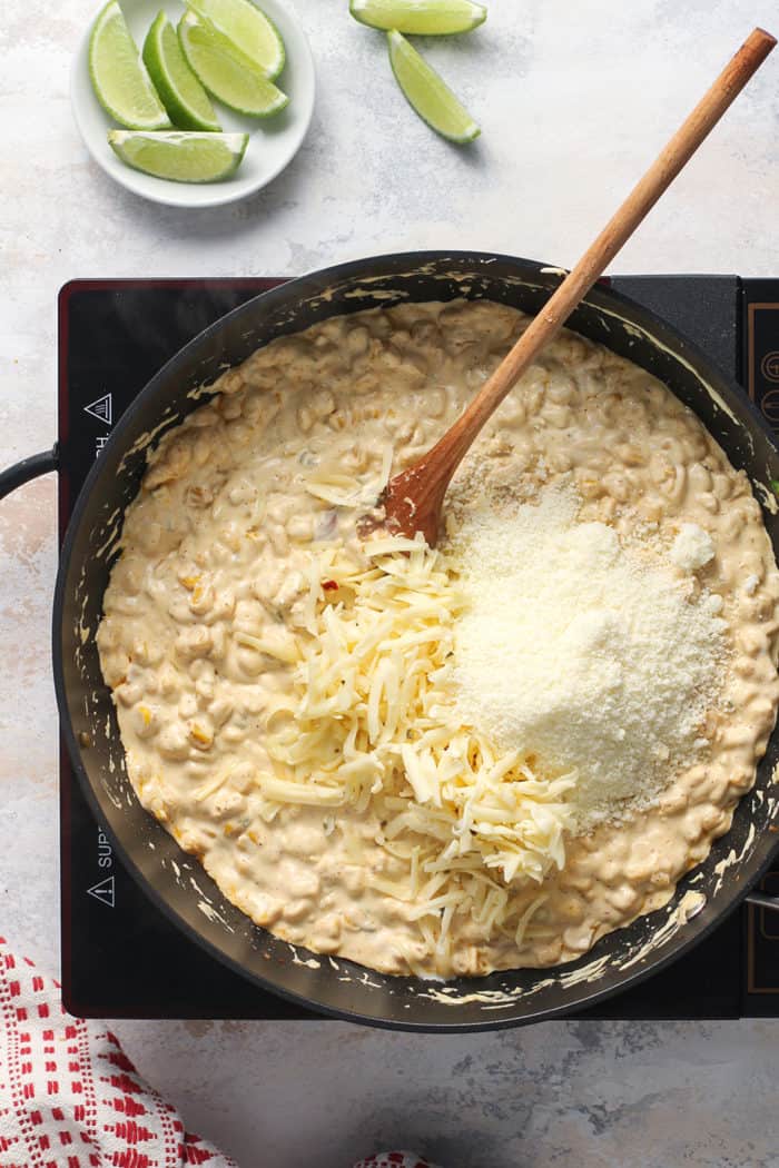 Shredded cheese being added to corn dip in a black skillet