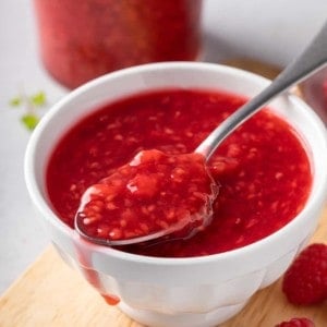 White bowl filled with raspberry sauce with a spoon holding some of the sauce set across the top