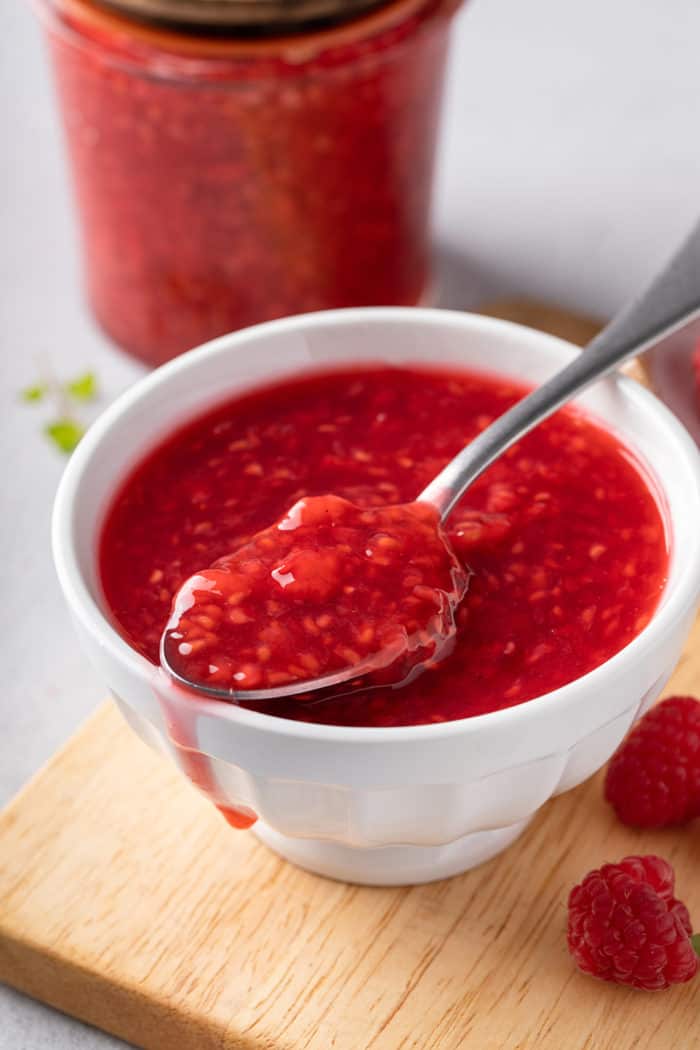 White bowl filled with raspberry sauce with a spoon holding some of the sauce set across the top