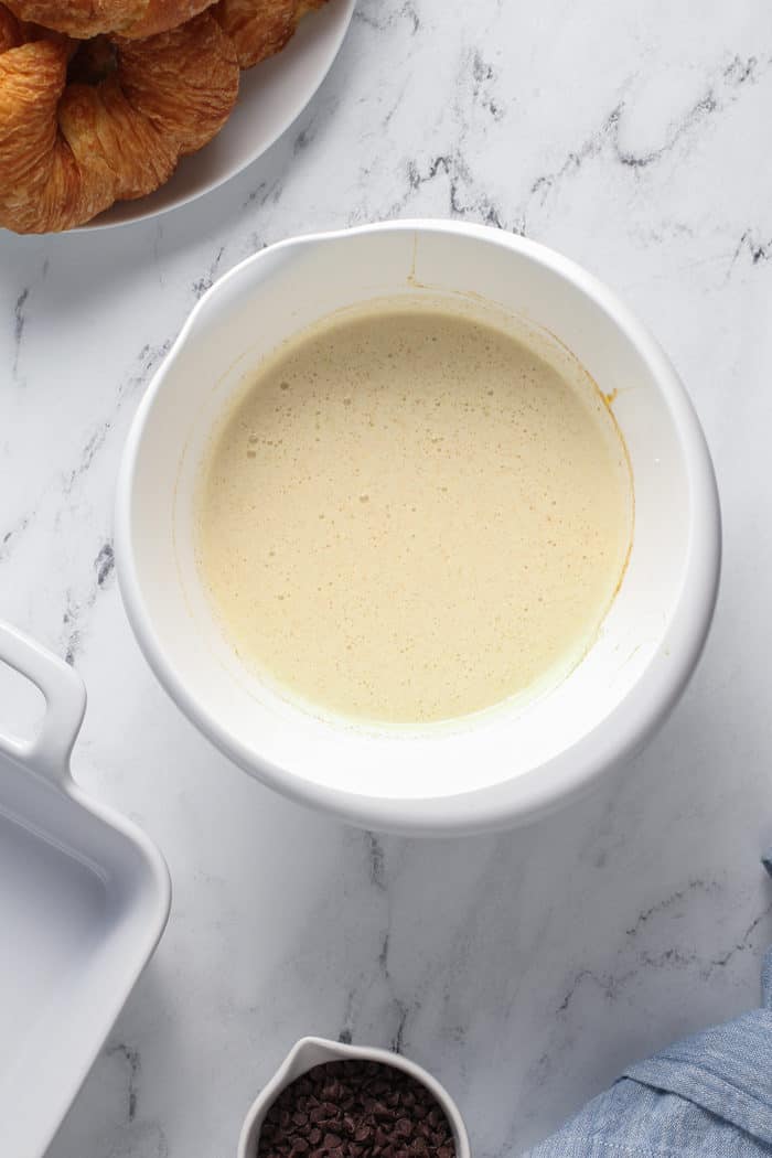 Custard for bread pudding in a white mixing bowl on a marble countertop