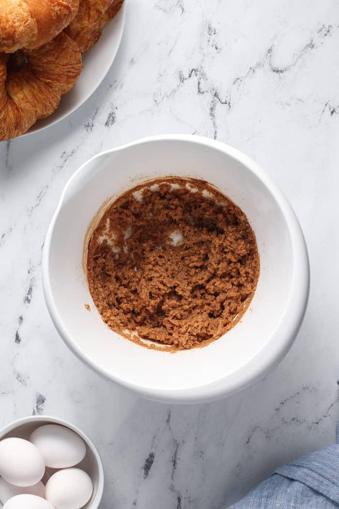 Butter, sugar, and cinnamon mixed together in a white mixing bowl set on a marble countertop