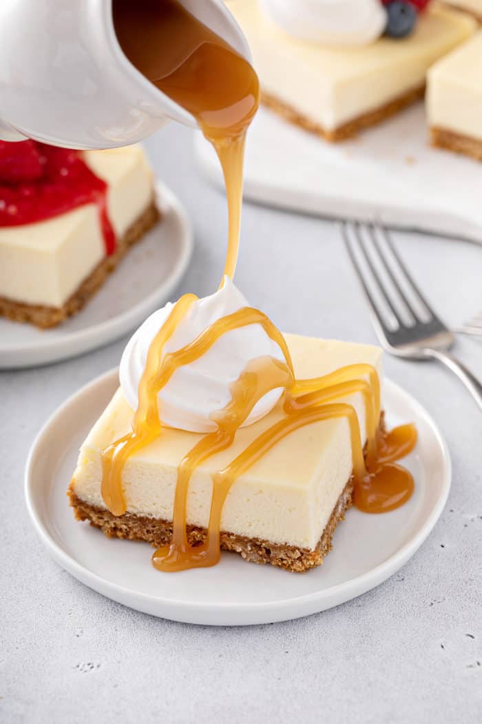 Caramel sauce being drizzled on top of a sliced cheesecake bar