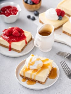 Plated cheesecake bars topped with various toppings: caramel, raspberry sauce, and fresh fruit