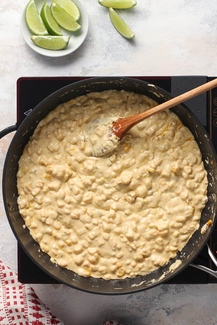 Wooden spoon stirring corn and diced jalapeños in a black skillet