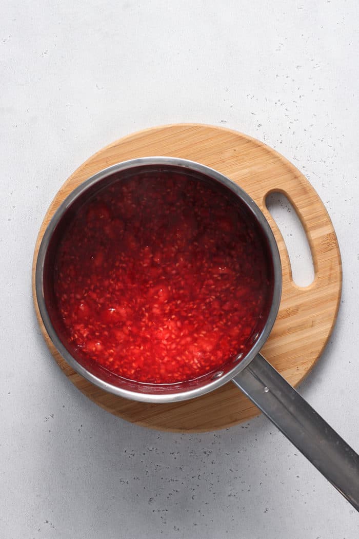 Overhead view of cooked raspberry sauce in a metal saucepan set on a wooden trivet