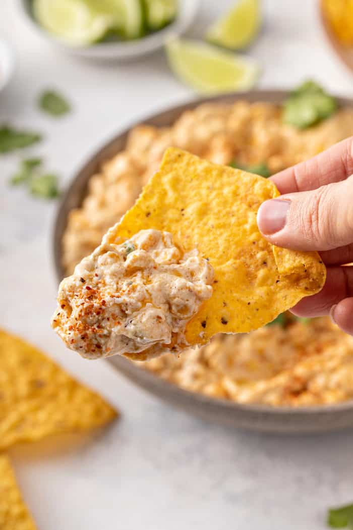 Hand holding up a tortilla chip with corn dip on it