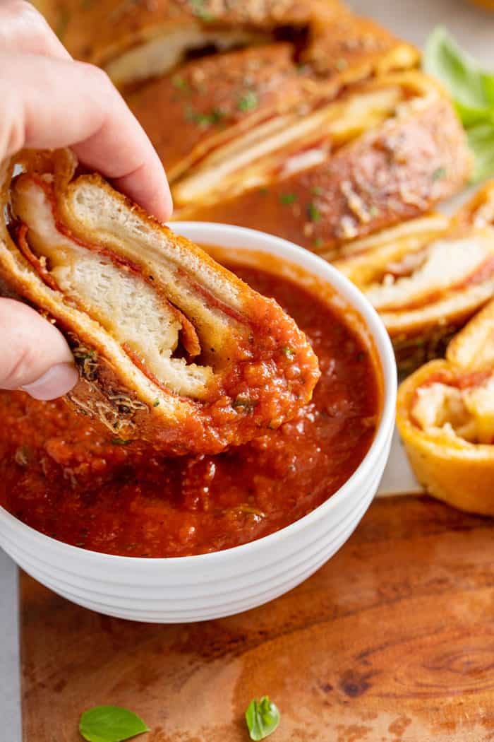 Piece of pepperoni bread being dipped into a bowl of tomato sauce