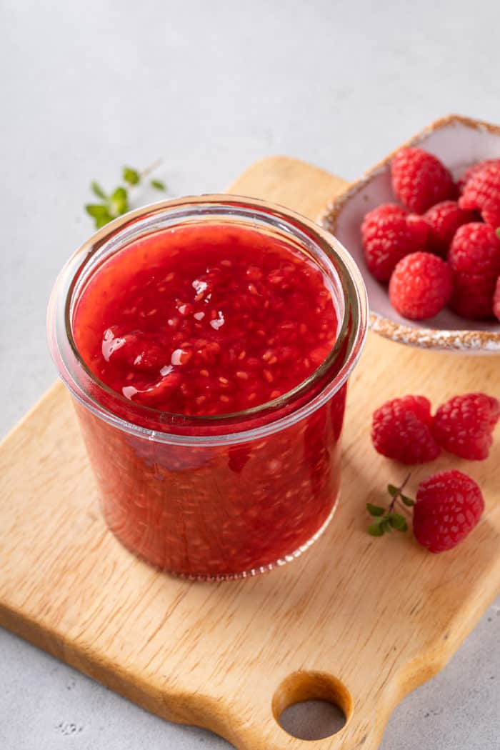 Glass jar filled with raspberry sauce set on a wooden board