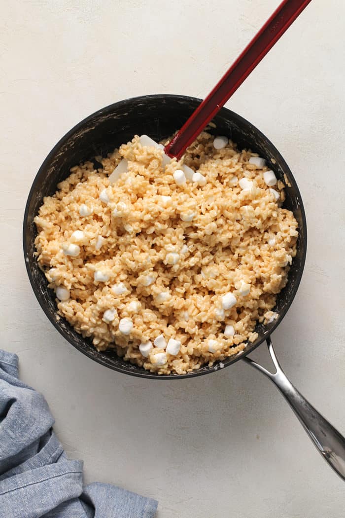 Spatula stirring rice krispie treat mix in a black high-walled skillet