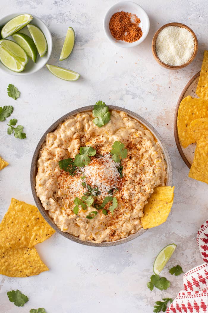 Overhead view of corn dip in a serving bowl, surrounded by tortilla chips and lime wedges