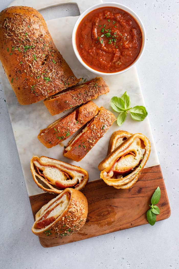 Overhead view of a sliced loaf of pepperoni bread next to a bowl of tomato sauce