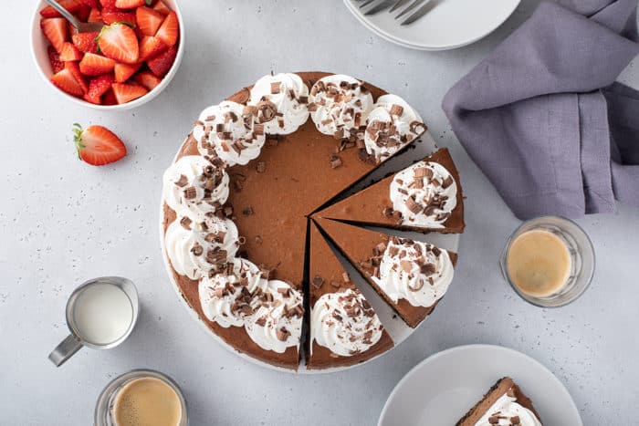 Overhead view of a sliced chocolate cheesecake topped with whipped cream and chocolate shavings