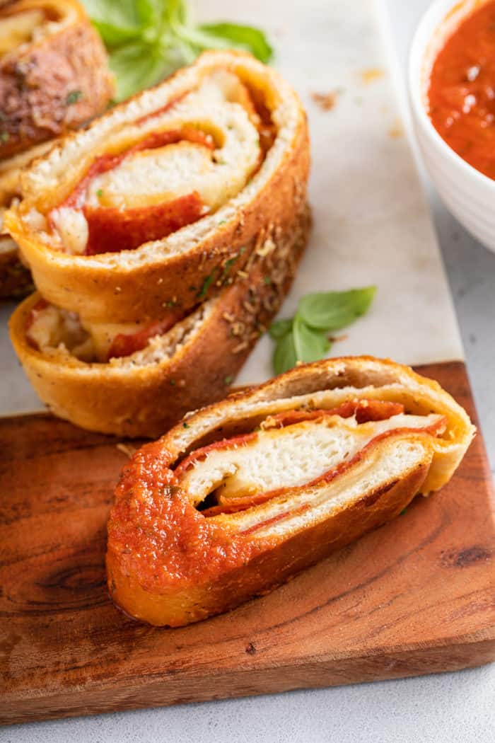 Slice of pepperoni bread dipped in pizza sauce, set on a marble and wood board