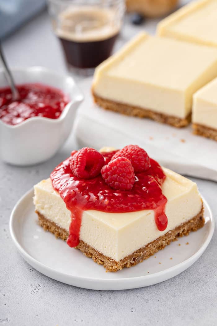 Cheesecake topped with raspberry sauce and fresh raspberries set on a white plate