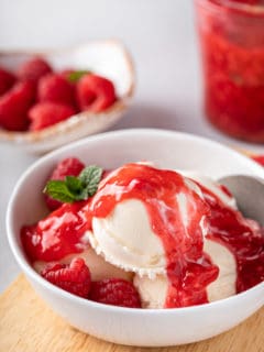 Close up of scoops of vanilla ice cream topped with raspberry sauce in a white bowl