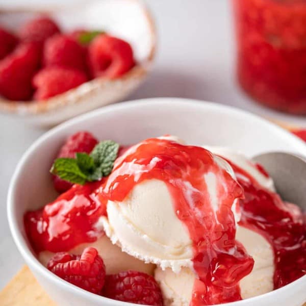 Close up of scoops of vanilla ice cream topped with raspberry sauce in a white bowl