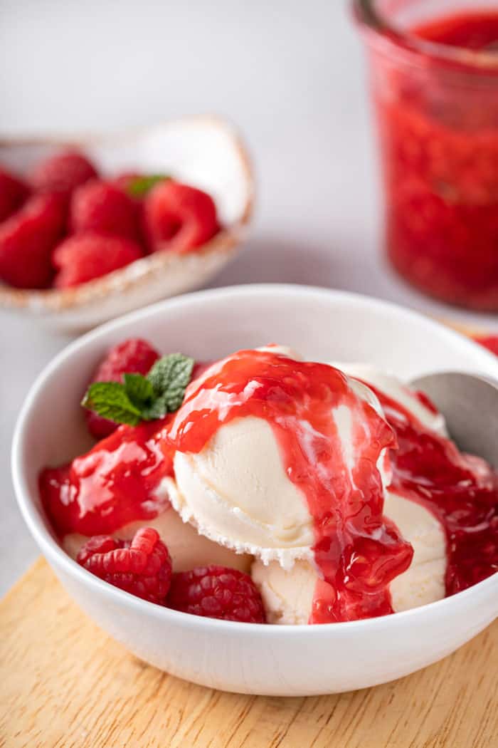 Close up of scoops of vanilla ice cream topped with raspberry sauce in a white bowl