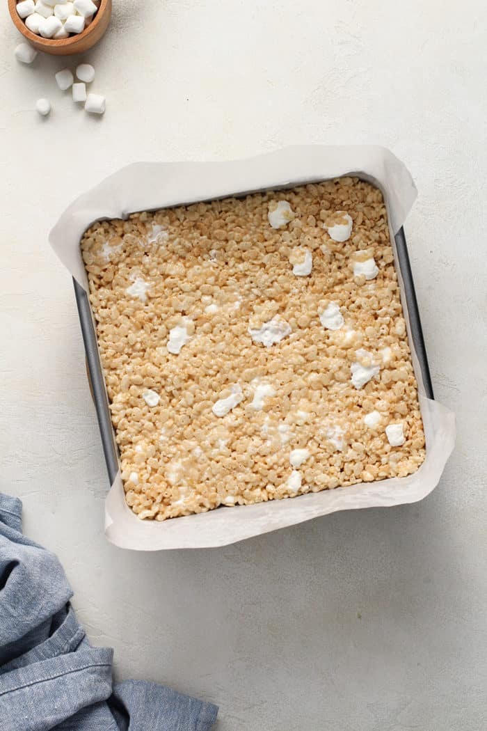 Classic rice krispie treats pressed into a parchment-lined square baking pan, set on a white countertop