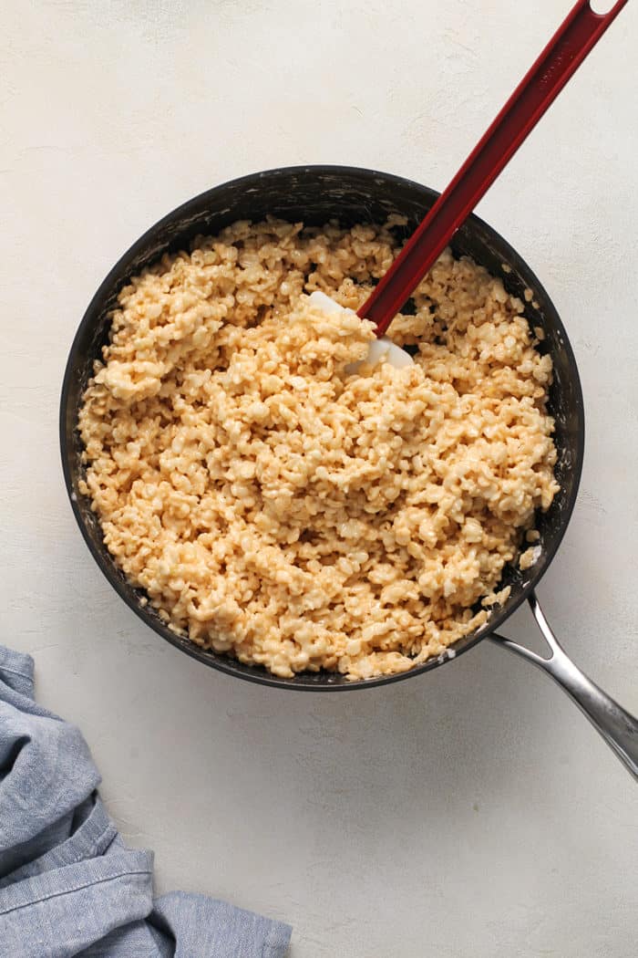 Spatula stirring rice krispies into melted marshmallows in a saucepan