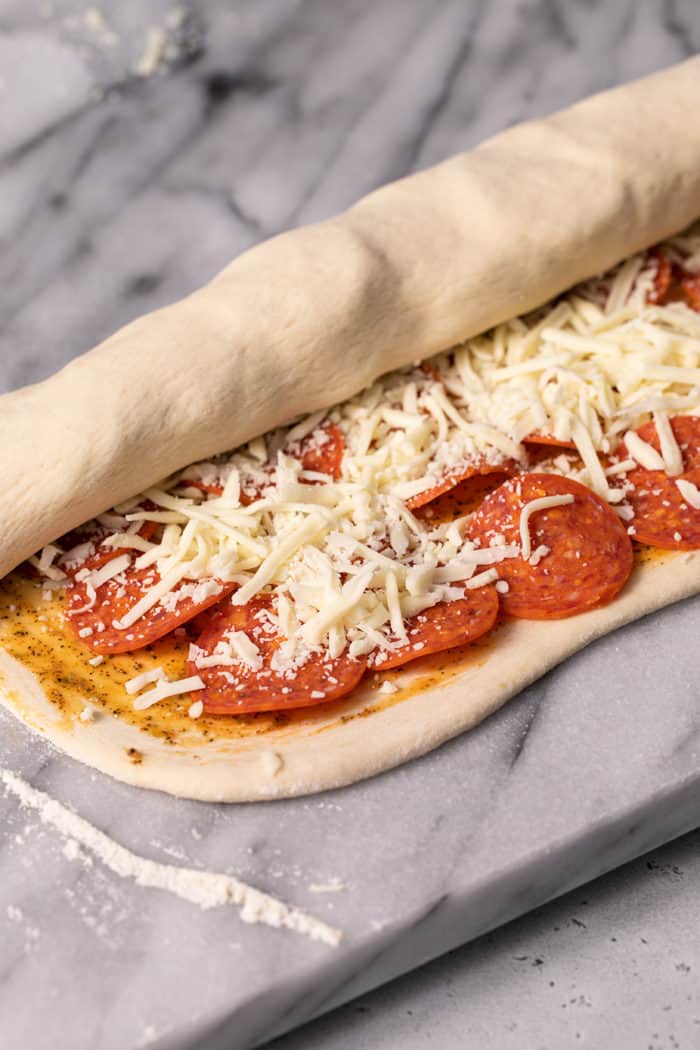 Loaf of pepperoni bread being rolled on a marble slab