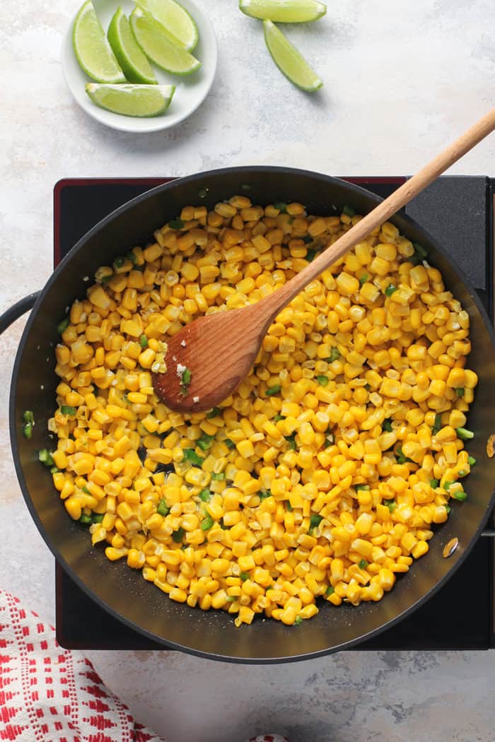 Wooden spoon stirring corn and diced jalapeños in a black skillet