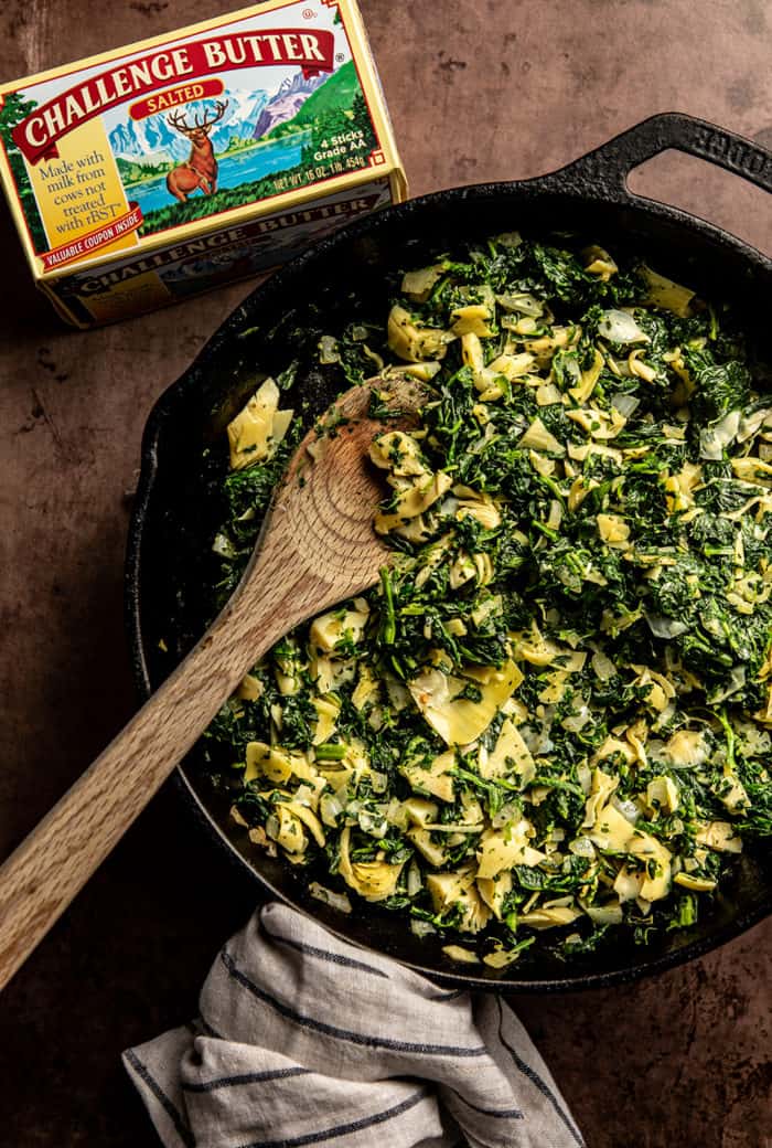 Wooden spoon stirring sauteed spinach and artichoke hearts in a skillet