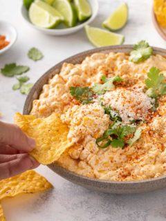Hand dipping a tortilla chip into a serving bowl of corn dip
