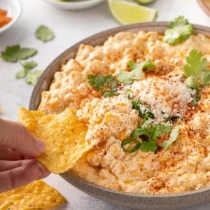 Hand dipping a tortilla chip into a serving bowl of corn dip