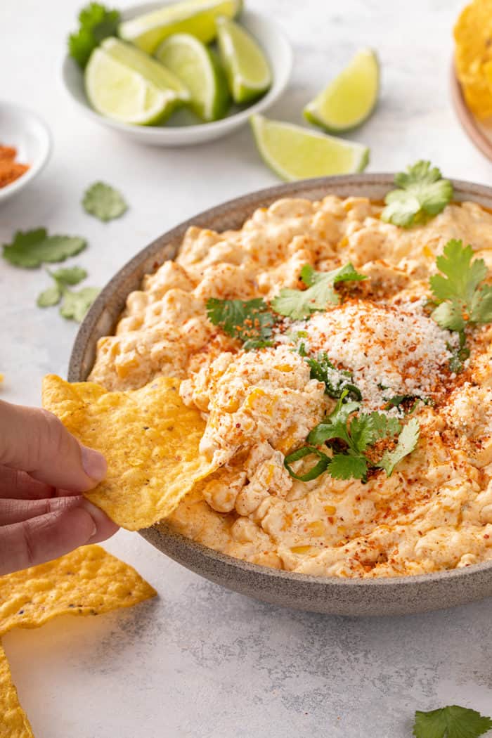 Hand dipping a tortilla chip into a serving bowl of corn dip