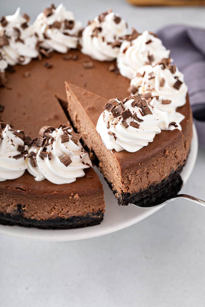 Cake server removing a slice of chocolate cheesecake from a whole cheesecake