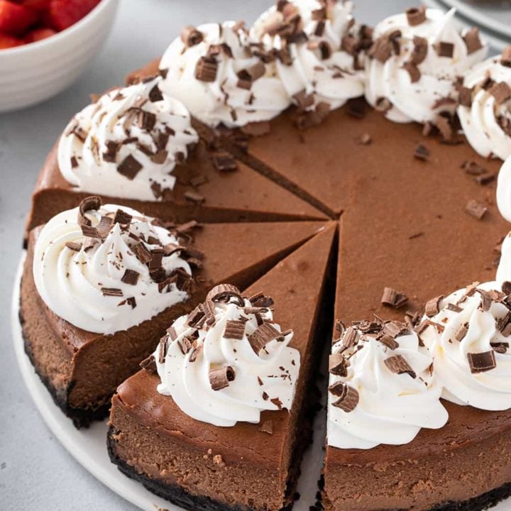 Sliced chocolate cheesecake topped with whipped cream on a white cake plate