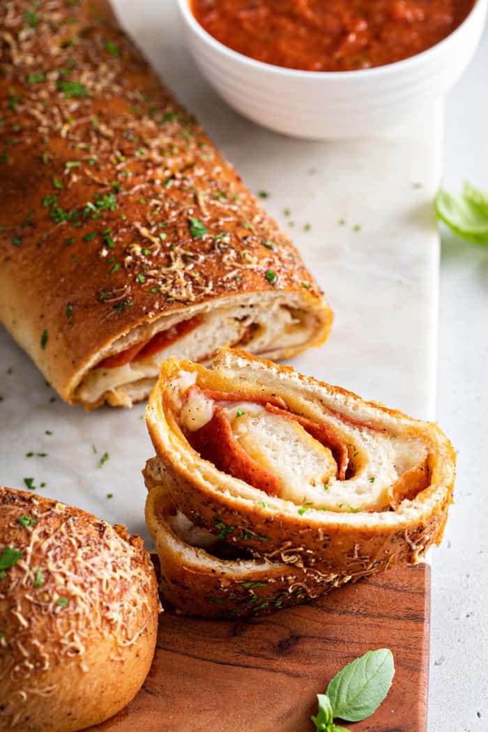 Slices cut from a loaf of pepperoni bread, set next to a bowl of pizza sauce